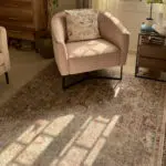 The Bustan Rug with intricate floral patterns in beige, blue, and red tones, styled in a cozy corner with a blush accent chair and wooden furniture.