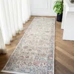 The Bustan Runner Rug with intricate floral patterns in beige, blue, and red tones, styled in a bright hallway with wooden flooring and natural decor.