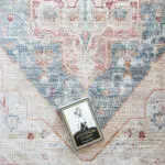 Detailed view of the Ishtar Medallion Rug in Dusty Azure with an artistic medallion pattern, paired with a decorative book for scale.