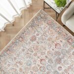 Corner view of the Bustan Rug featuring intricate floral patterns and a decorative border in beige, blue, and red tones, styled in a bright living space.