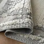 Close-up of the Mist Haven Rug folded to display its plush gray and cream texture and durable edge stitching.