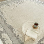 Close-up view of the Mist Haven Rug, paired with a marble coffee table, showcasing its soft gray and cream tones with distressed detailing.