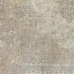 Close-up of the Regency Royal Carpet’s ornate border, showcasing intricate scrolling patterns and floral motifs in beige, gold, and subtle blue accents on a distressed background.