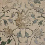Close-up of Seraphic Carpet showcasing intricate floral patterns in gold, blue, and green on a soft beige background.